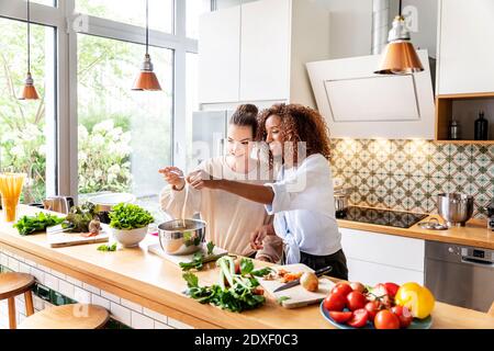 Female coworkers cooking spaghetti together at work place kitchen Stock Photo