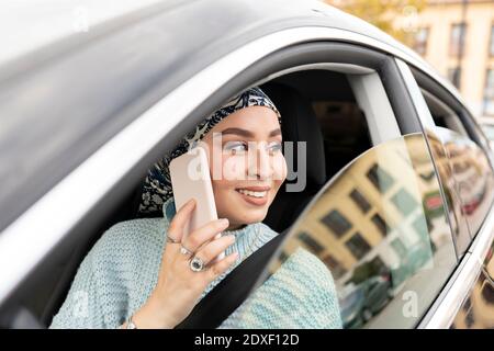 Young woman talking on mobile phone while sitting in car at city Stock Photo