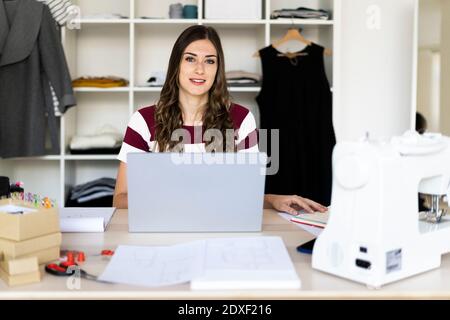 Young female fashion designer sitting with laptop in studio Stock Photo