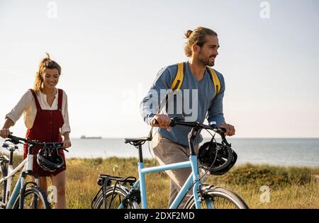 Smiling man and woman with bicycles walking against clear sky Stock Photo
