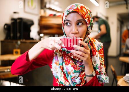 Malaysian woman looking away while drinking coffee in cafe Stock Photo