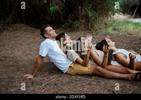 Cheerful family doing yoga while lying down in row at forest during vacation Stock Photo