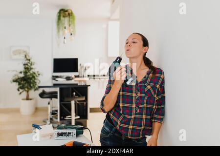 Woman holding electric drill while leaning on wall at home Stock Photo