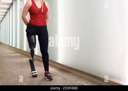 Sportswoman with prosthetic leg walking by wall in underpass Stock Photo