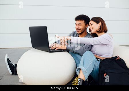 Smiling couple sitting and using laptop on white concrete ball Stock Photo