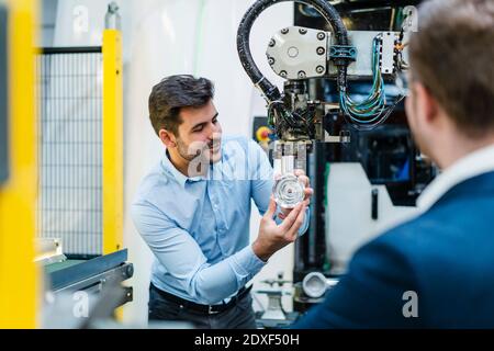 Male entrepreneur explaining about machine part to manager at industry Stock Photo