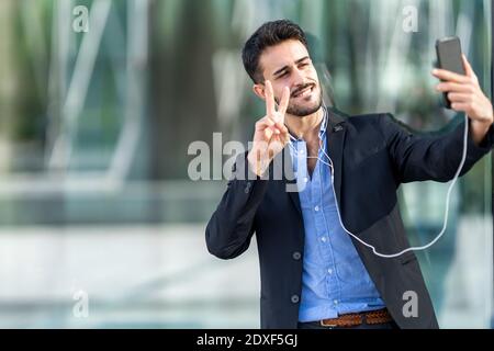 Confident businessman showing peace sign while taking selfie Stock Photo