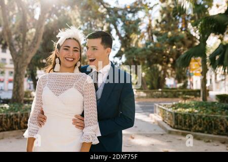 Smiling groom embracing bride while standing in park Stock Photo