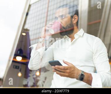 Candid portrait of bearded businessman drinking coffee and using phone inside cafe Stock Photo