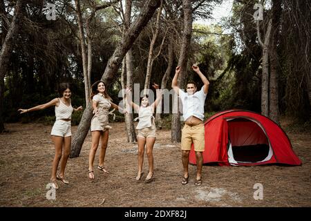 Cheerful family jumping in forest against at campsite during vacation Stock Photo
