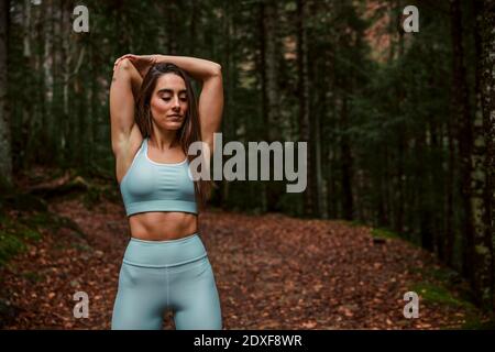 Sportswoman stretching arms while standing with eyes closed in forest Stock Photo