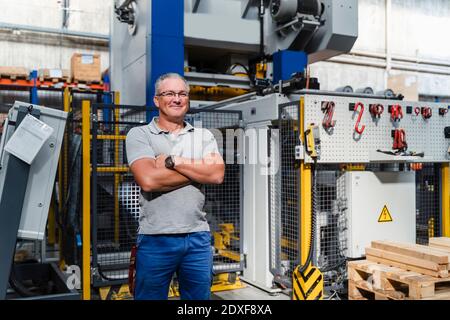 Male manual worker smiling confidently with arms crossed at illuminated industry Stock Photo