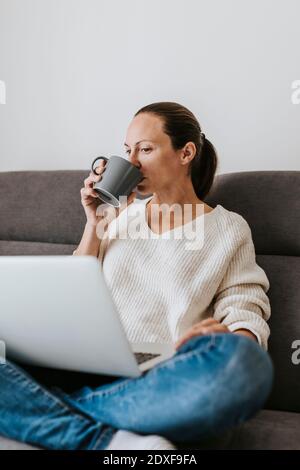 Woman drinking coffee while using laptop at home Stock Photo