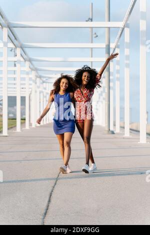 Smiling young female friends walking with arms around Stock Photo