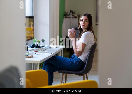 Businesswoman holding coffee cup while sitting on chair at office Stock Photo