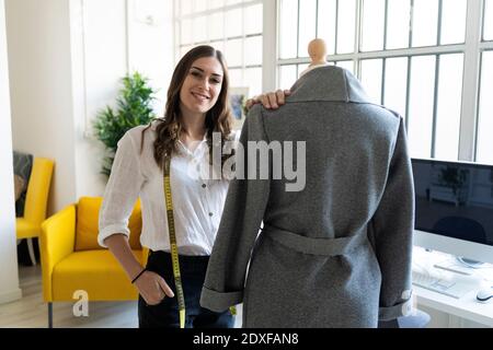 Smiling fashion designer standing by mannequin in studio Stock Photo