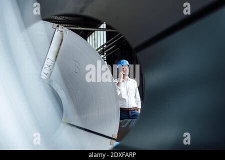 Businessman talking on smart while standing at factory Stock Photo