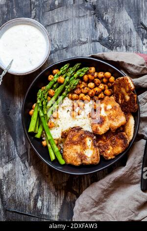 Dipping sauce and bowl of rice with chick-peas, asparagus stalks and fried halloumi cheese Stock Photo