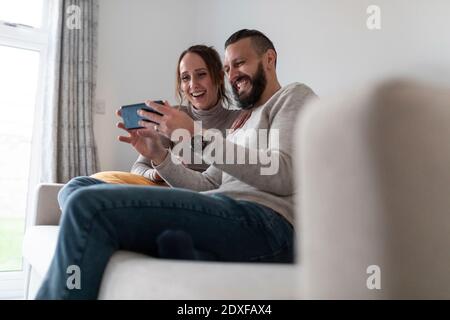 Happy couple using smart phone while sitting at home Stock Photo