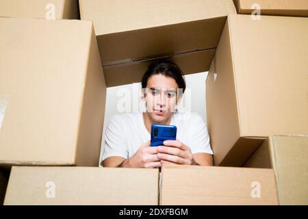 Man using mobile phone while leaning on cardboard boxes Stock Photo