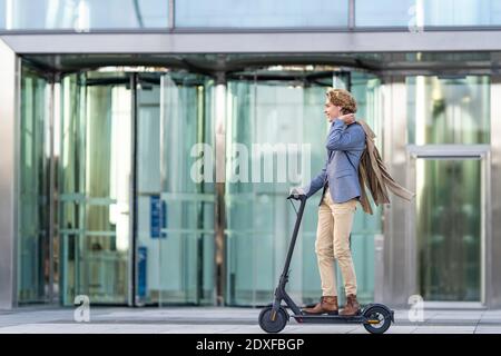 Young businessman riding electric push scooter on footpath Stock Photo