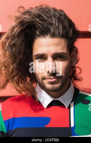 Young man with long hair standing against red wall Stock Photo