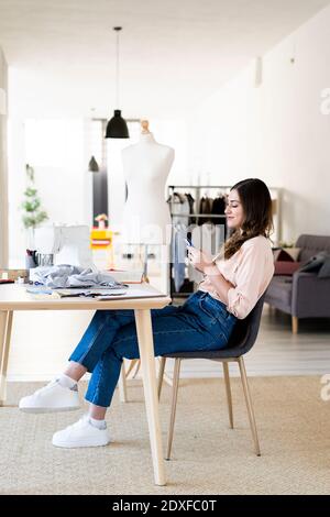 Young female designer using smart phone while sitting on chair at studio Stock Photo