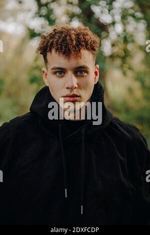 Young man wearing hooded shirt staring while standing at park Stock Photo