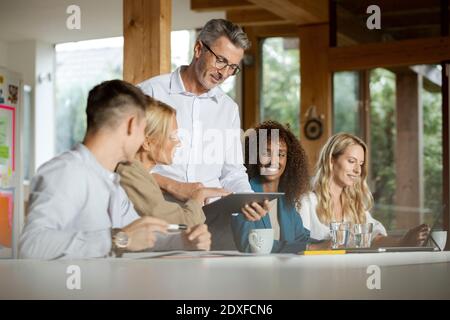 Businessman using digital tablet while standing by colleagues in meeting at office Stock Photo