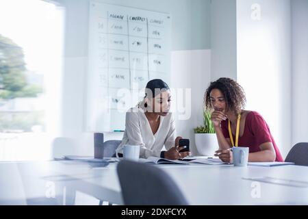 Female colleagues using smart phone while sitting at desk in office Stock Photo