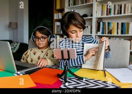 Boy attending video lecture through smart phone sitting with male friend at home Stock Photo