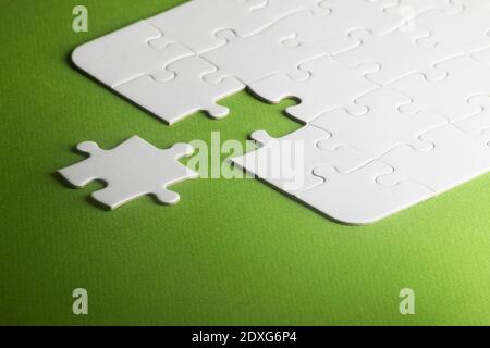 A white puzzle with one piece missing but not fitting. green background, copy space Stock Photo