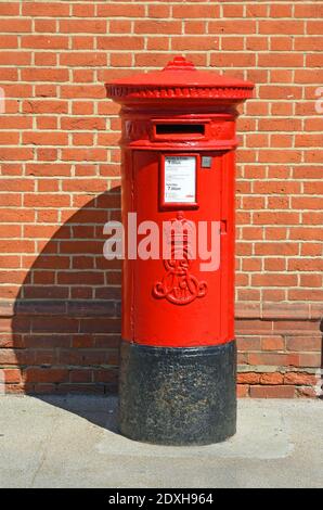 Red post box isolated against brick wall. Stock Photo