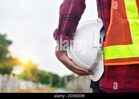 Close up hand holding white hard hat safety Engineer Technician Against Sky background Stock Photo