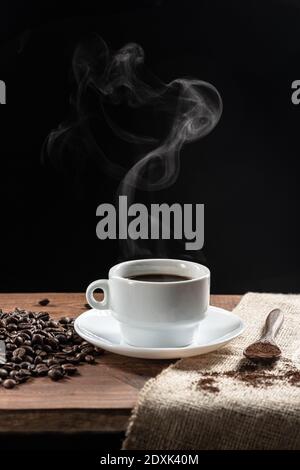 Warm coffe smoke, with  coffee beans. wooden spoon with coffe on wooden base, on dark background. Stock Photo