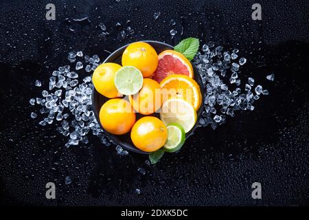 Citrus dish whith orange, lemon, lime and grapefruit with ice and mint on fresh wet black background. Top view. Stock Photo