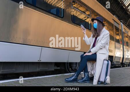 Girl sitting on the platform of the train station and using smartphone Stock Photo