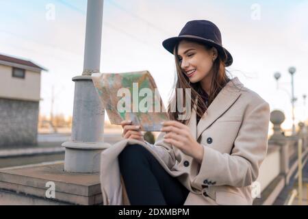Tourist woman sits and looks at map of the city. Girl prefers to use paper map for orientation in the city Stock Photo
