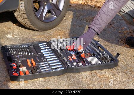 Сar driver using different repair tools for repairing a car. Tool set near the orange auto. Closeup picture of mechanic tools in box. Stock Photo