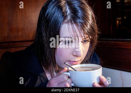 A beautiful young woman Fiona Donaldson enjoying a cup of coffee on a cold February morning inside the Fisher & Donaldson traditional Scottish bakery and Continental confectionery and cake shop in Dundee, UK Stock Photo