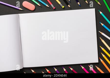 Various colored pencils and sketchbook on a black background with copy space, top view. Stock Photo