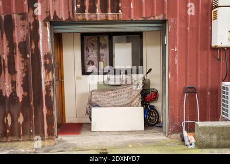 Hsinchu / Taiwan - March 20, 2020: Entrance door of metallic wall poor house in Hsinchu with electric bike and Minnie Mouse poster Stock Photo