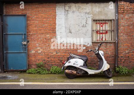 Hsinchu / Taiwan - March 20, 2020: Old rusty scooter next to brick wall house Stock Photo