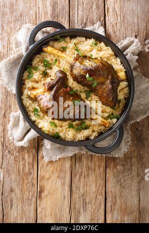 Yemeni dish of baked lamb shank served with aromatic rice close-up in a frying pan on the table. vertical top view from above Stock Photo