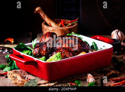 Baked chicken in glaze with vegetables in red form for baking on old wooden table, rustic style, selective focus Stock Photo