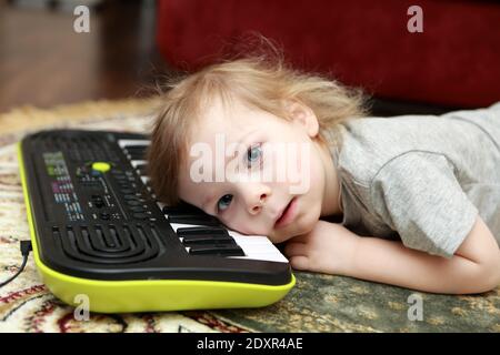 Kid lying and playing on synthesizer at home Stock Photo