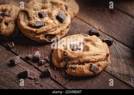 Closeup of a chocolate chip cookie with cookies in background and chocolate pieces on a rustic wooden table Stock Photo