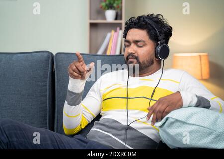 Young man listening peaceful music at home while lying on sofa - concept of music lover, lazy weekend relaxation and modern lifestyle. Stock Photo