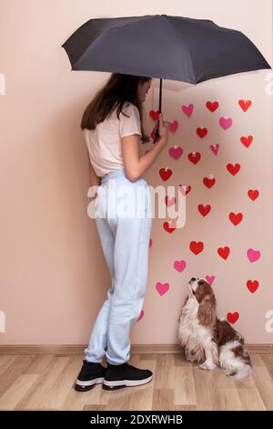 Young fashion woman girl holding an umbrella guarding her love from the rain with red hearts. Photo in full growth, dog pet cavalier king charles span Stock Photo