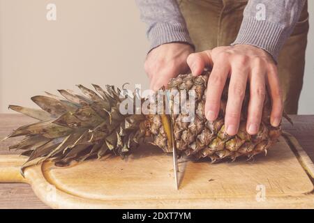 Man hands cutting a pineapple on a wooden table Stock Photo